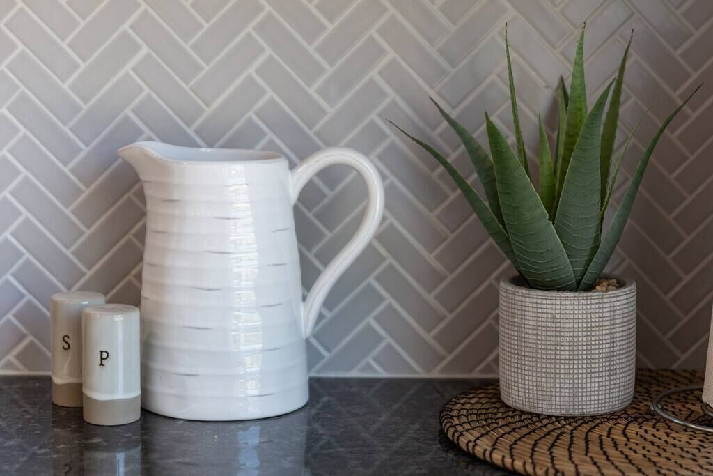 A kitchen counter with a white pitcher, two salt and pepper shakers, and a potted plant.