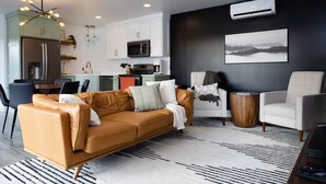 A modern living room with a sofa, chairs, a coffee table, and a kitchen in the background.
