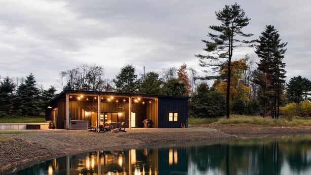 A cabin with a large deck and a pond in front.