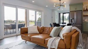 A modern living room with a leather sofa, a dining table, and a kitchen area.