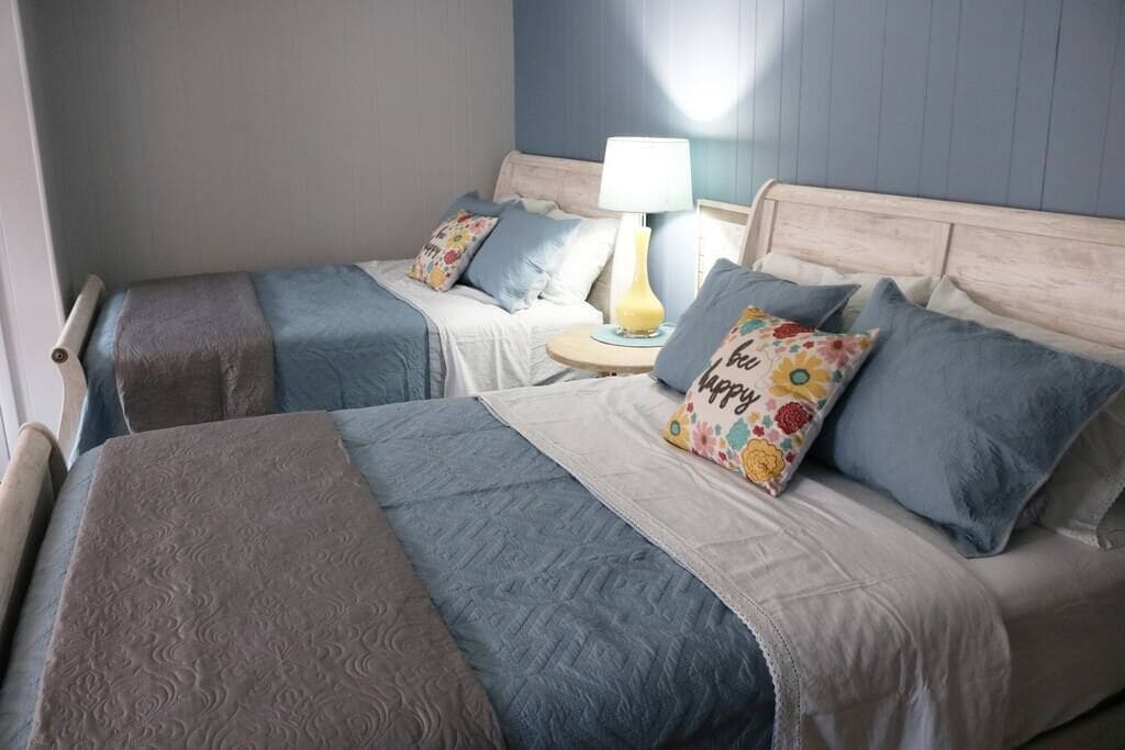 A twin bedroom with two beds, a bedside table with a lamp, and a floral pillow.