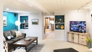 Sala de estar con sofá, mesa de centro y televisor. Se observa una cocina al fondo.