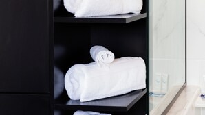 A bathroom with a black shelf holding rolled white towels, a potted plant, and a glass shower enclosure.