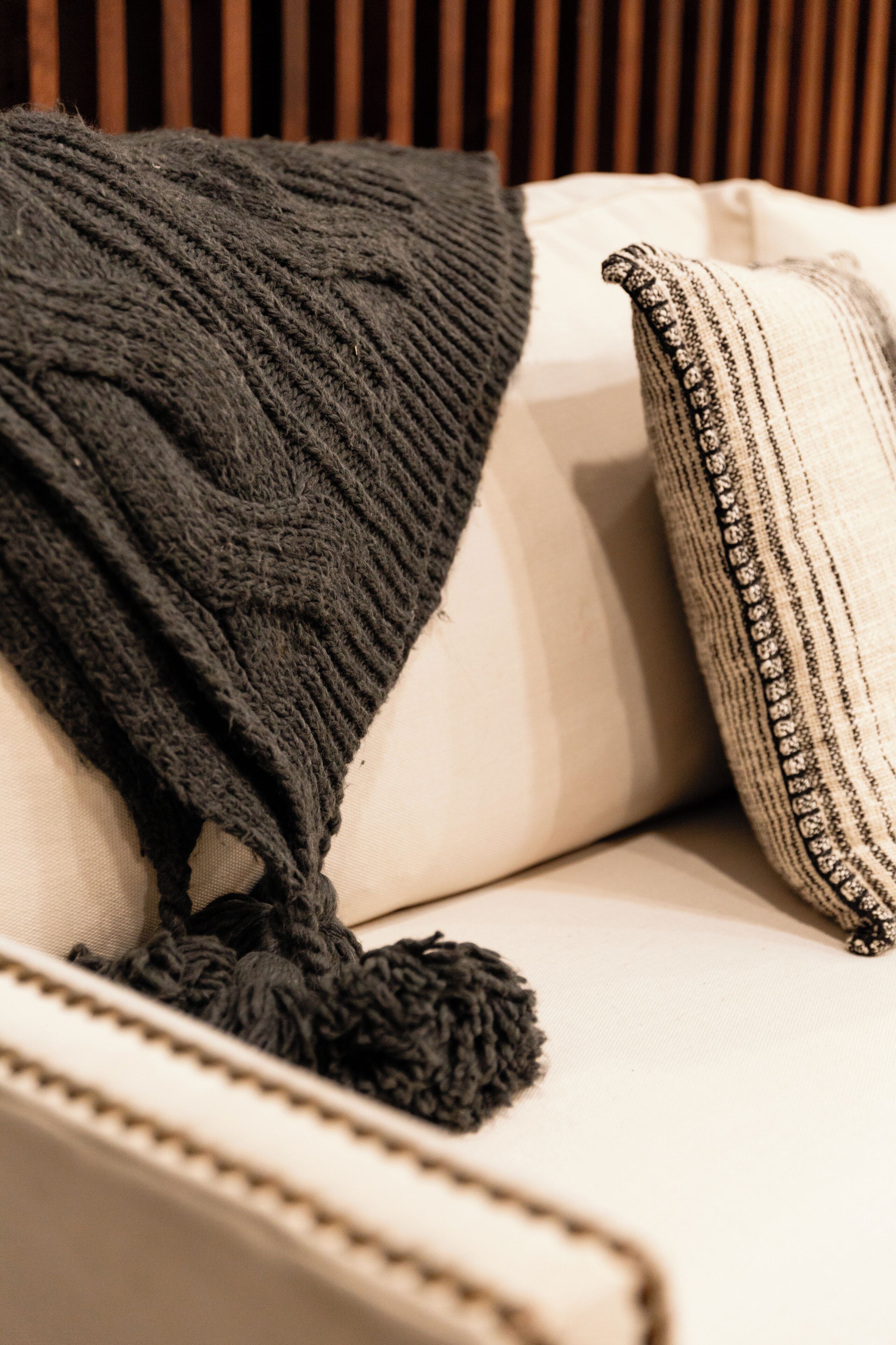 Gros plan d’un canapé recouvert d’un plaid tricoté foncé et agrémenté d’un coussin à rayures.