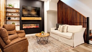 A modern living room with a sofa, a recliner, a coffee table, a fireplace, and a TV.