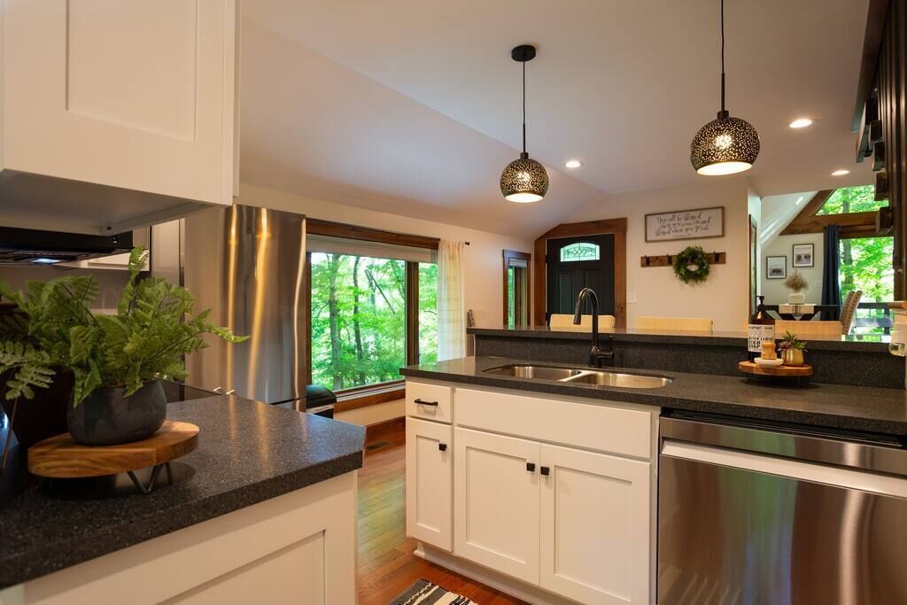 A modern kitchen with white cabinets, stainless steel appliances, and a large window offering a view of greenery.