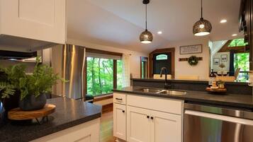 A modern kitchen with white cabinets, stainless steel appliances, and a large window offering a view of greenery.