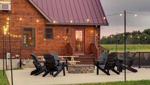 Una cabaña rústica con chimenea de piedra, mobiliario exterior e iluminación con luces colgantes.