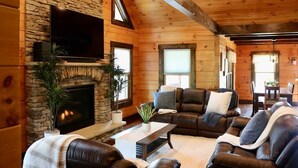 Interior acogedor de una cabaña de troncos con chimenea de piedra, sofás de cuero y un televisor de pantalla plana montado en la pared.