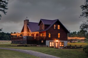 Una casa grande de dos pisos con fachada de ladrillo y techo de metal, que cuenta con un porche iluminado con luces y una chimenea visible.