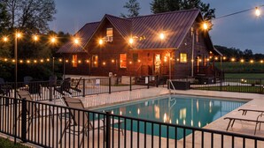 Una cabaña rústica con piscina, mobiliario exterior e iluminación colgante.