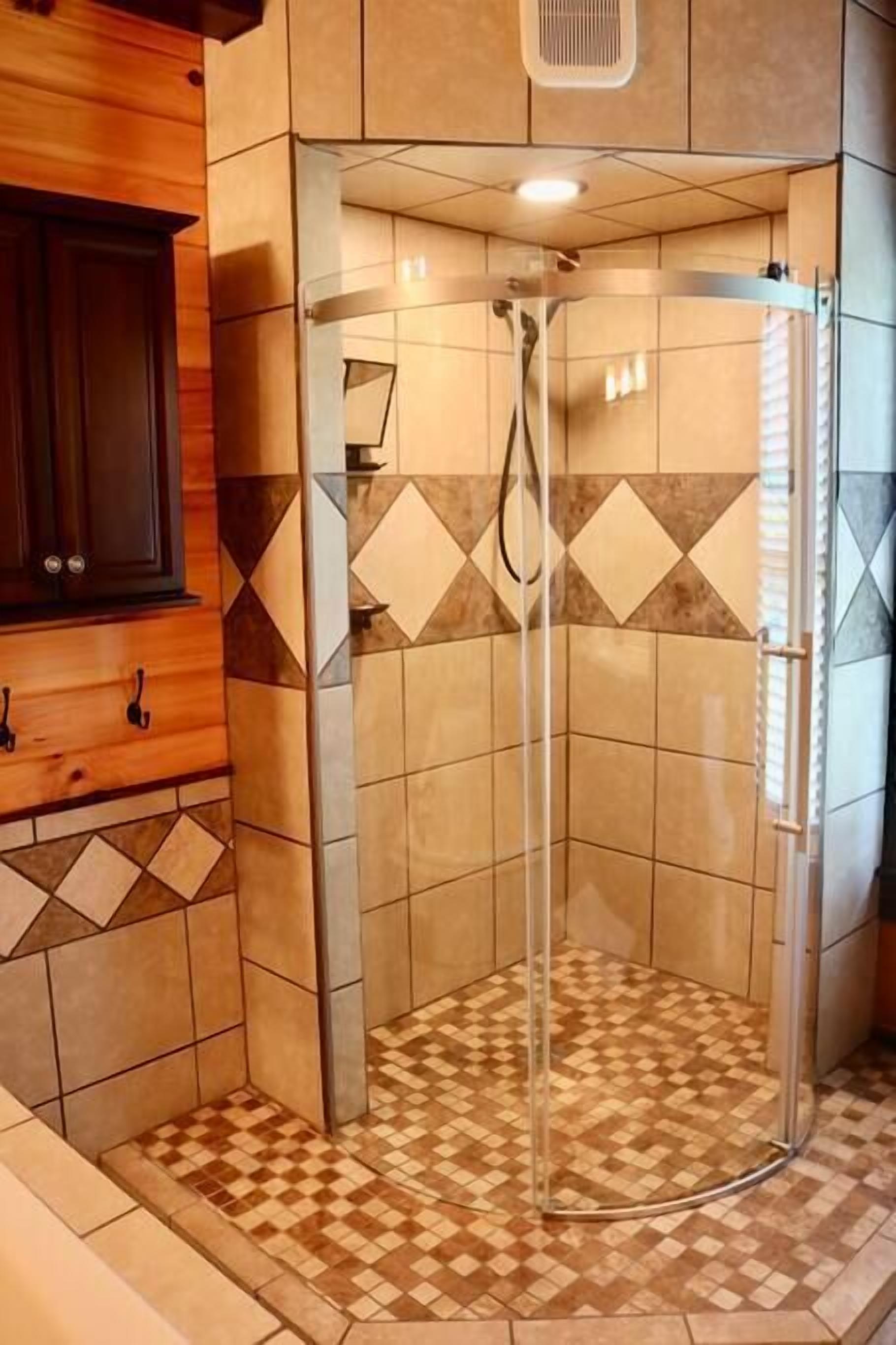 Un espace douche doté d’une porte en verre, de murs carrelés et d’un sol à motifs à carreaux.