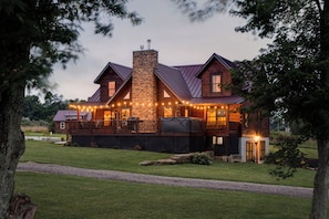 A two-story house with a stone chimney, wooden deck, and string lights. - Mohican Haven Lodge. (Union Township)