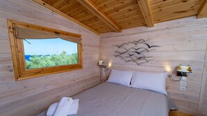 Un dormitorio de cabaña de madera con una cama, una ventana con vistas, una lámpara de pared y un enchufe.