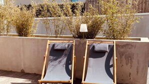 Two wooden lounge chairs with canvas seats and backrests, positioned on a wooden deck with a concrete wall and bamboo plants in the background. - Ground floor holiday apartment for 4 people (Saint-Pierre-Quiberon)
