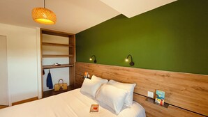 A bedroom with a bed, a wooden headboard, a green wall, and a hanging light fixture. - Ground floor holiday apartment for 4 people (Saint-Pierre-Quiberon)