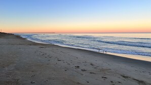 A beach with a pier extending into the water, sandy shore, and footprints in the sand. - Oceanside Home in Duck, NC, Private Pool & Hot Tub (Kitty Hawk)