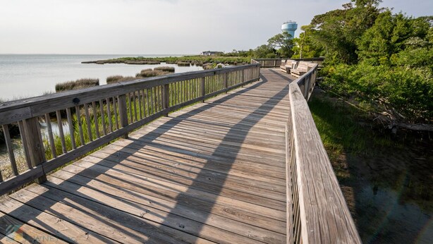 A wooden boardwalk leading to a water tower, surrounded by greenery and marshland. - Oceanside Home in Duck, NC, Private Pool & Hot Tub (Kitty Hawk)