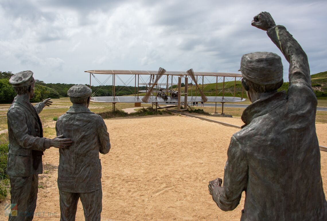 A statue of three figures in military attire, with a vintage biplane in the background.