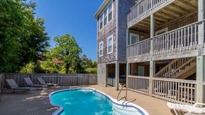 A swimming pool with lounge chairs, a wooden deck, and a two-story building with balconies. - Oceanside Home in Duck, NC, Private Pool & Hot Tub (Kitty Hawk)