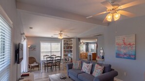 A living room with a sofa, coffee table, and ceiling fan. There is a dining area with chairs and a table. - Oceanside Home in Duck, NC, Private Pool & Hot Tub (Kitty Hawk)