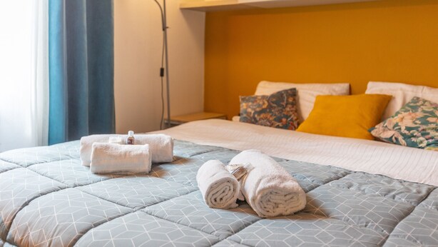 A neatly made bed with a geometric patterned duvet, a set of towels, and a bedside lamp. - -STUDIO ARENA (Verona)