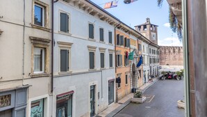 A narrow street with historic buildings, a clock tower, and outdoor seating. - -STUDIO ARENA (Verona)