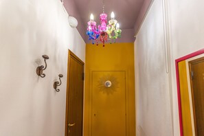 Un pasillo con una puerta amarilla, una pared blanca y una lámpara de araña colorida.