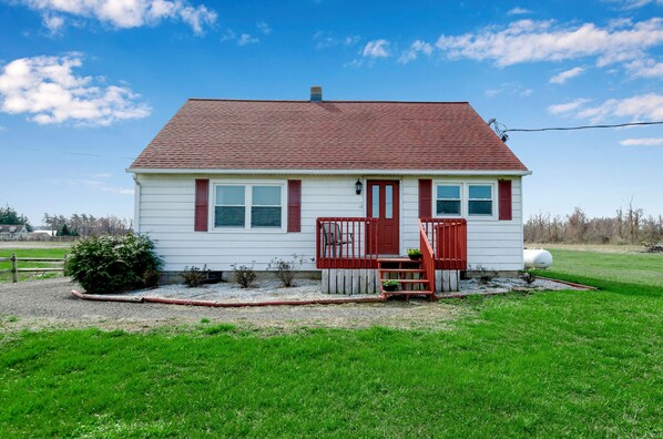 A single-story house with a red roof and white siding, a front porch with a red railing, and a small garden area.