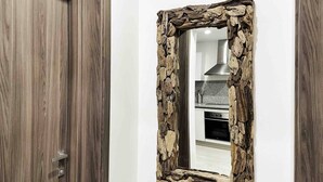 Een kamer met een houten deur, een spiegel met stenen lijst en een keukenhoek met witte kastjes en een roestvrijstalen afzuigkap.