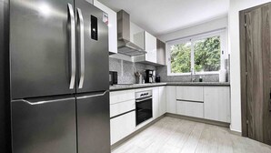 Een moderne keuken met roestvrijstalen apparatuur, witte kastjes en een groot raam dat voor daglicht zorgt.