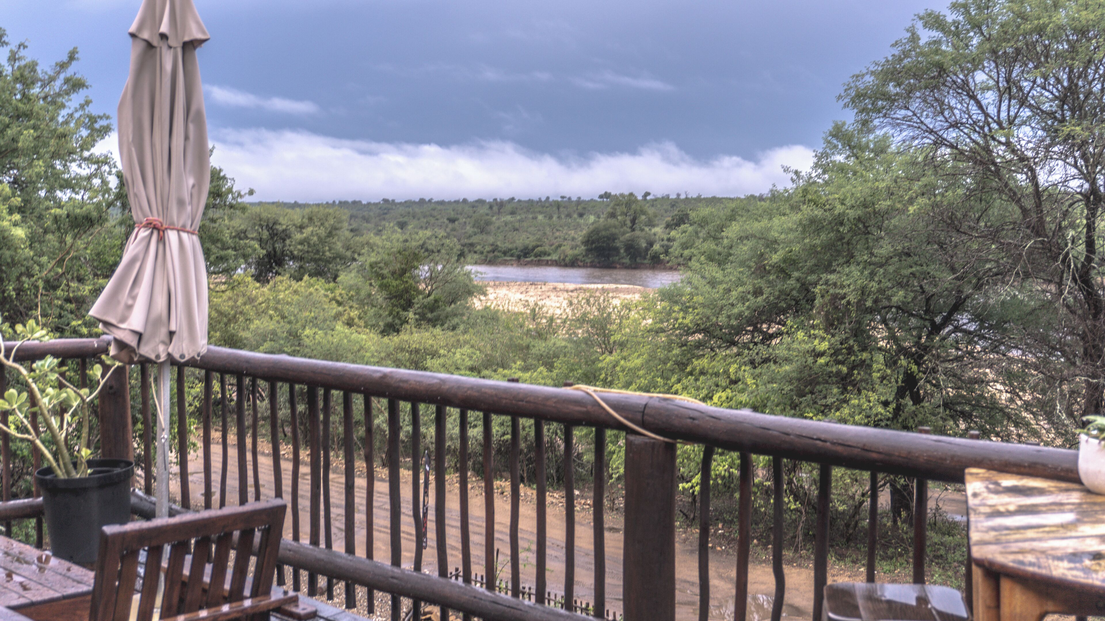 A wooden deck with a railing, overlooking a river and dense greenery.