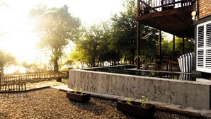 Un espacio exterior tranquilo con piscina de hormigón, terraza de madera y mobiliario.