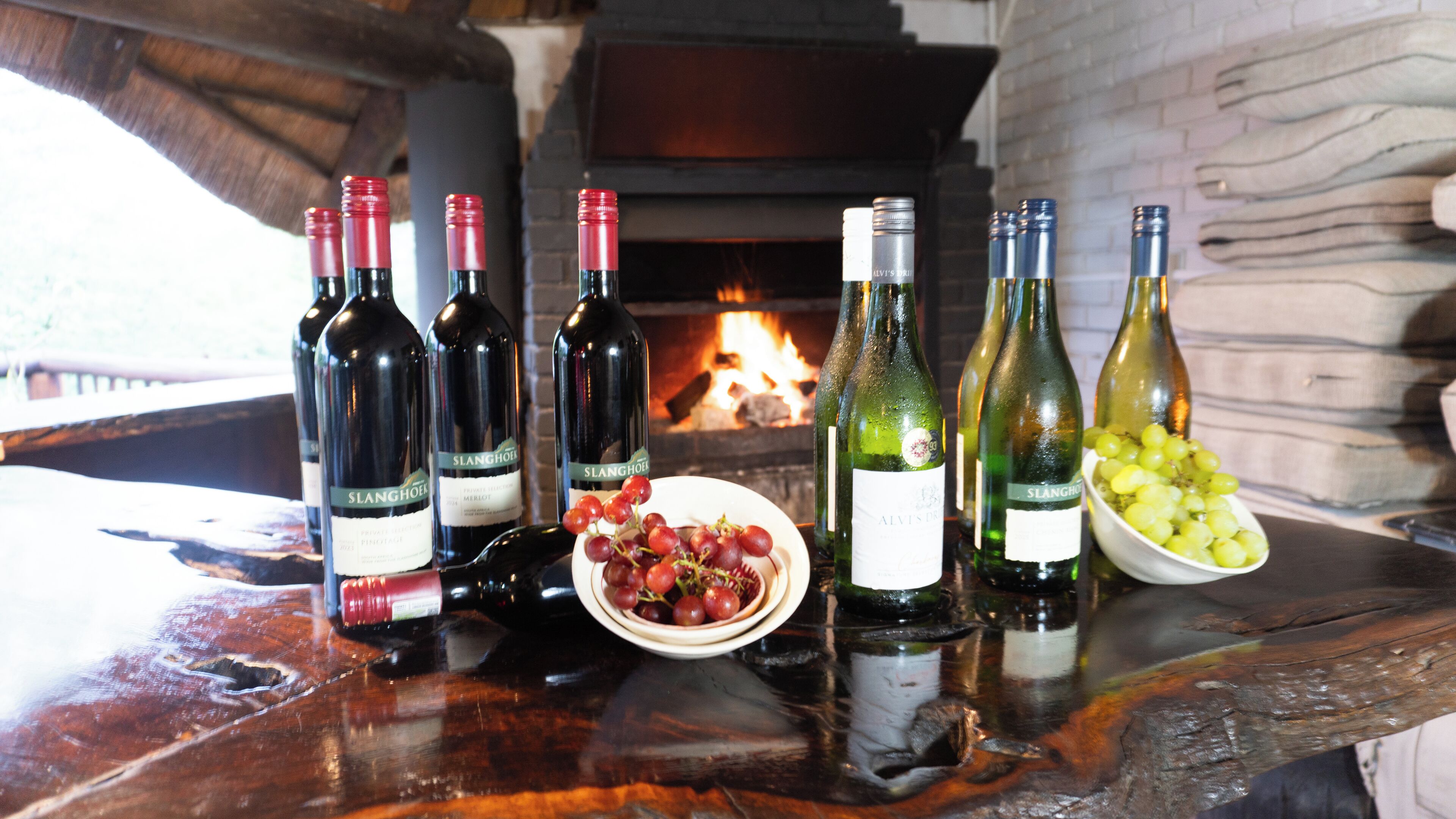 Varias botellas de vino sobre una mesa de madera, con una chimenea al fondo.