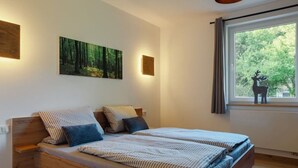 A double bed with striped bedding, a wooden headboard, and a forest-themed painting above it.