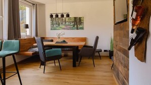 A dining area with a wooden table, four chairs, a bench, and a painting of a forest on the wall.