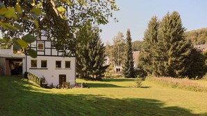 A white building with a black trim, a well-maintained lawn, and surrounding trees.