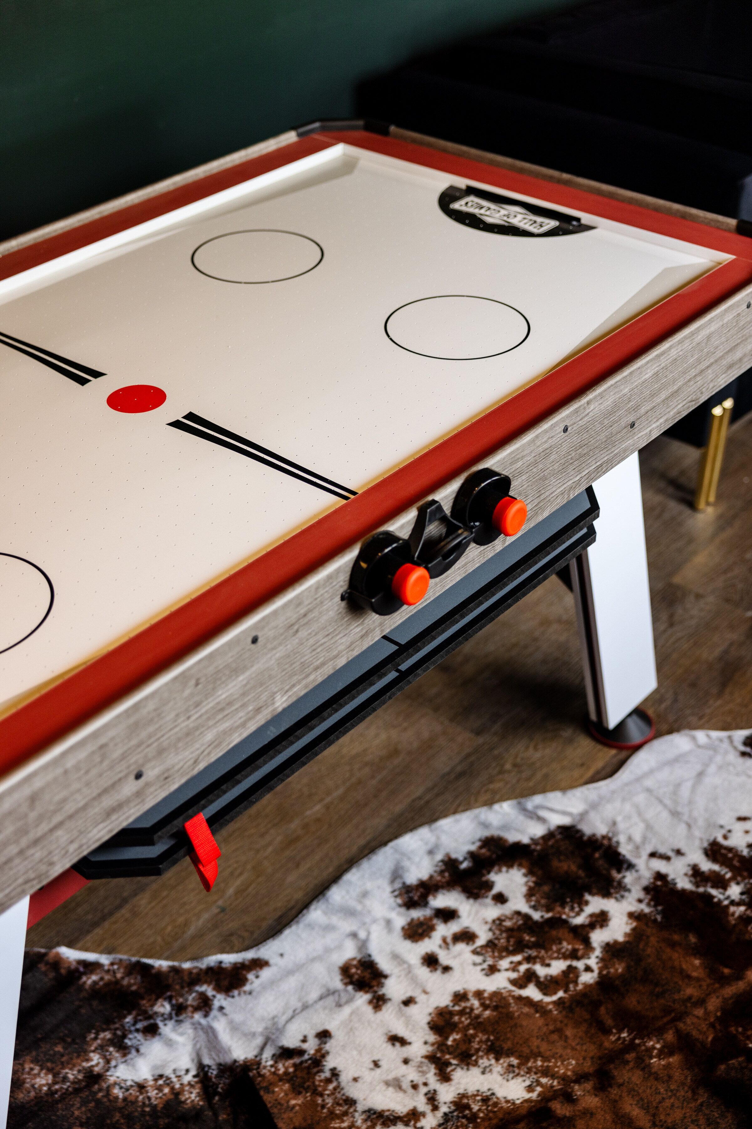 A foosball table with a wooden frame and red accents, positioned on a wooden floor.