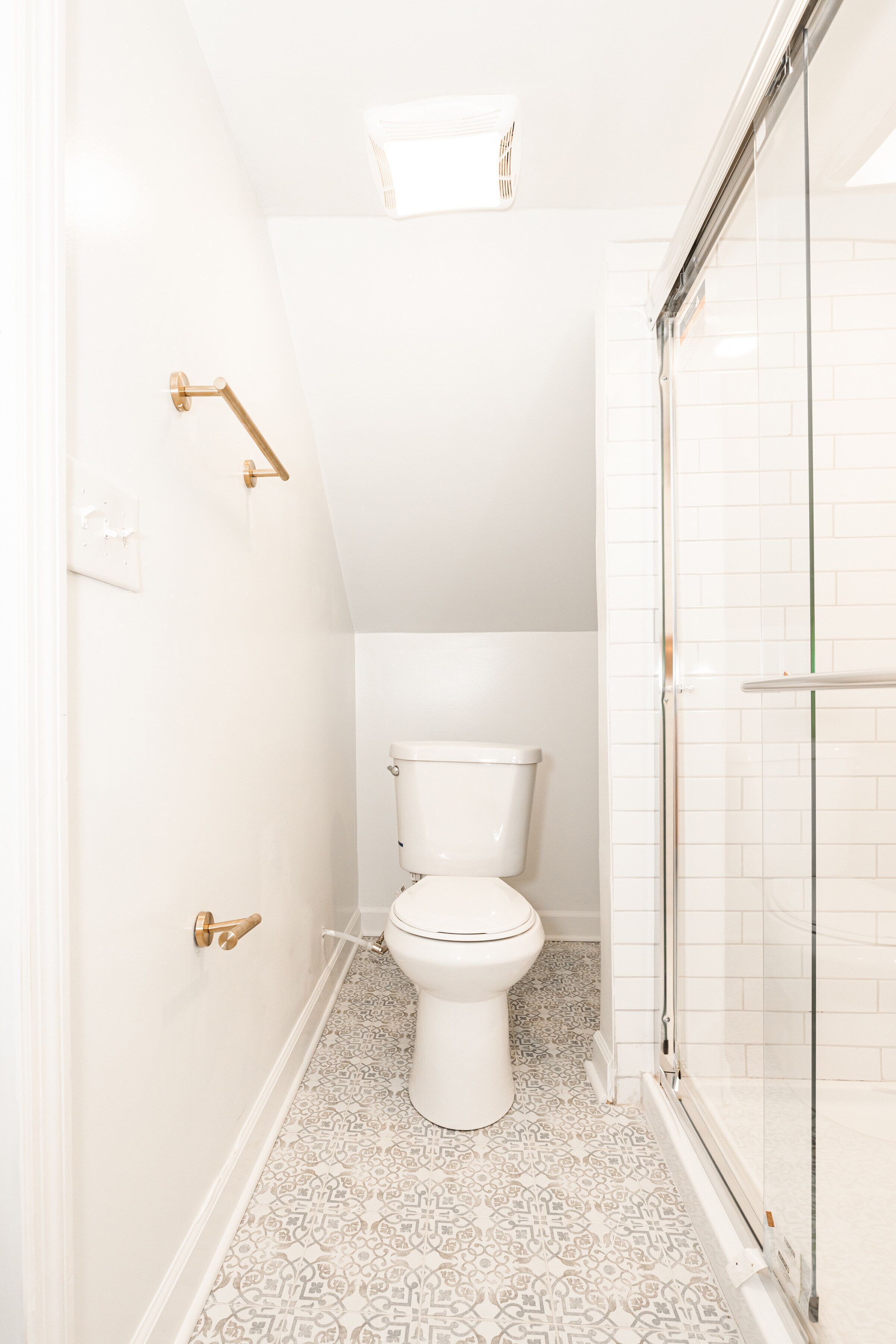 Un baño pequeño y blanco con inodoro, ducha y suelo estampado.