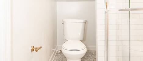 Un baño pequeño y blanco con inodoro, ducha y suelo estampado.