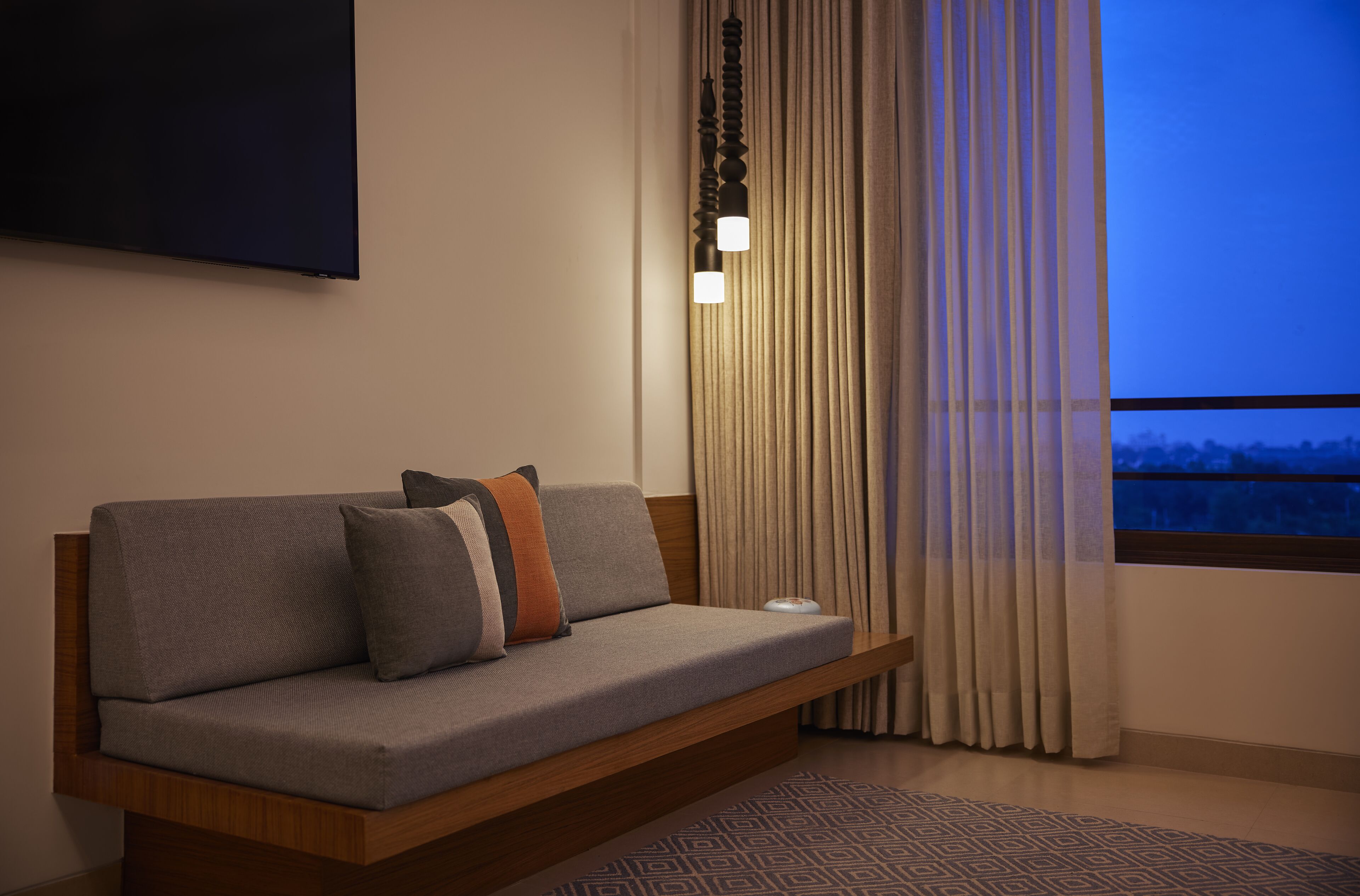 A modern sofa with cushions, a mounted TV, and a window with curtains.