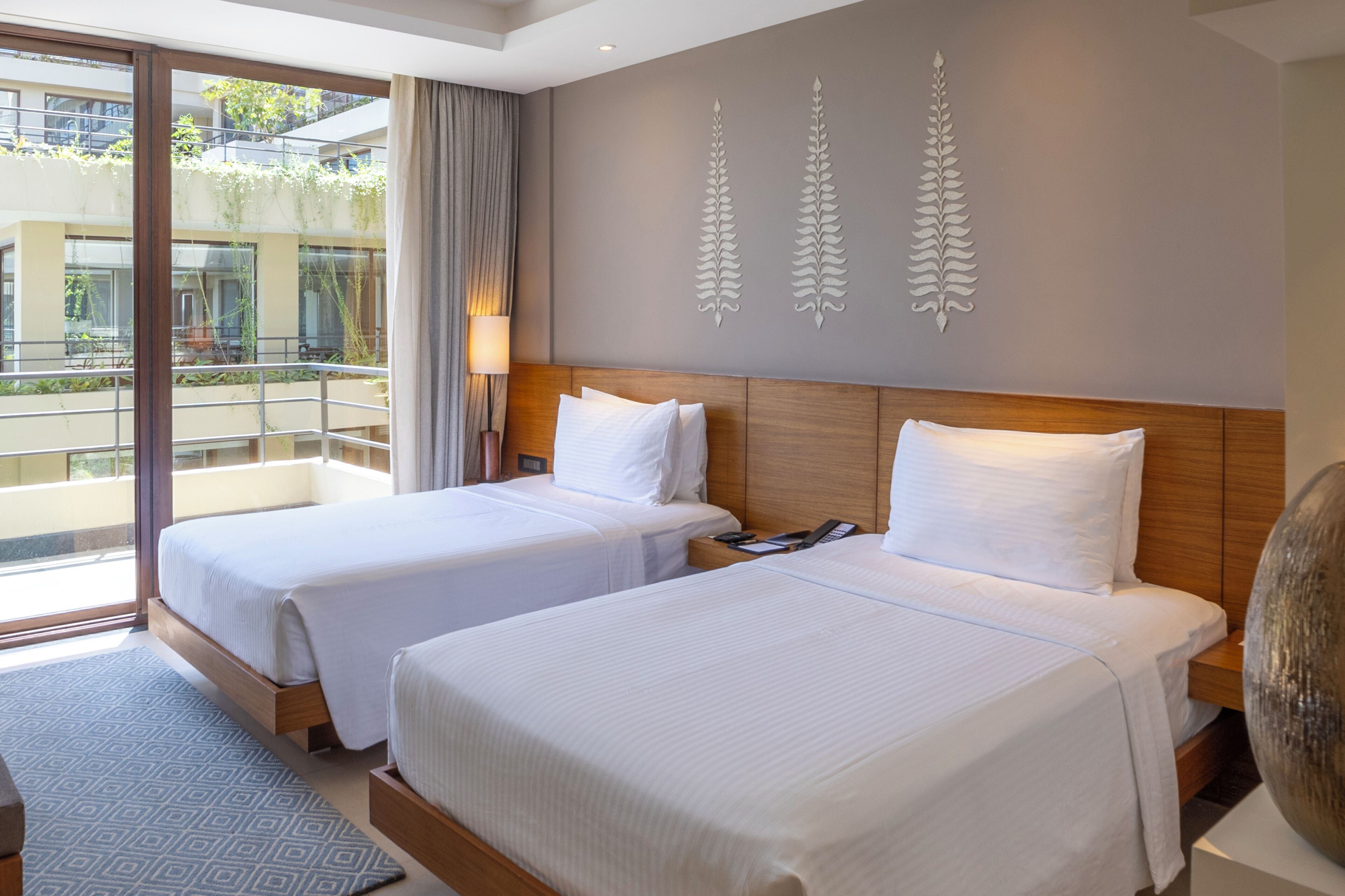 A hotel room with two beds, a large window, and a balcony.