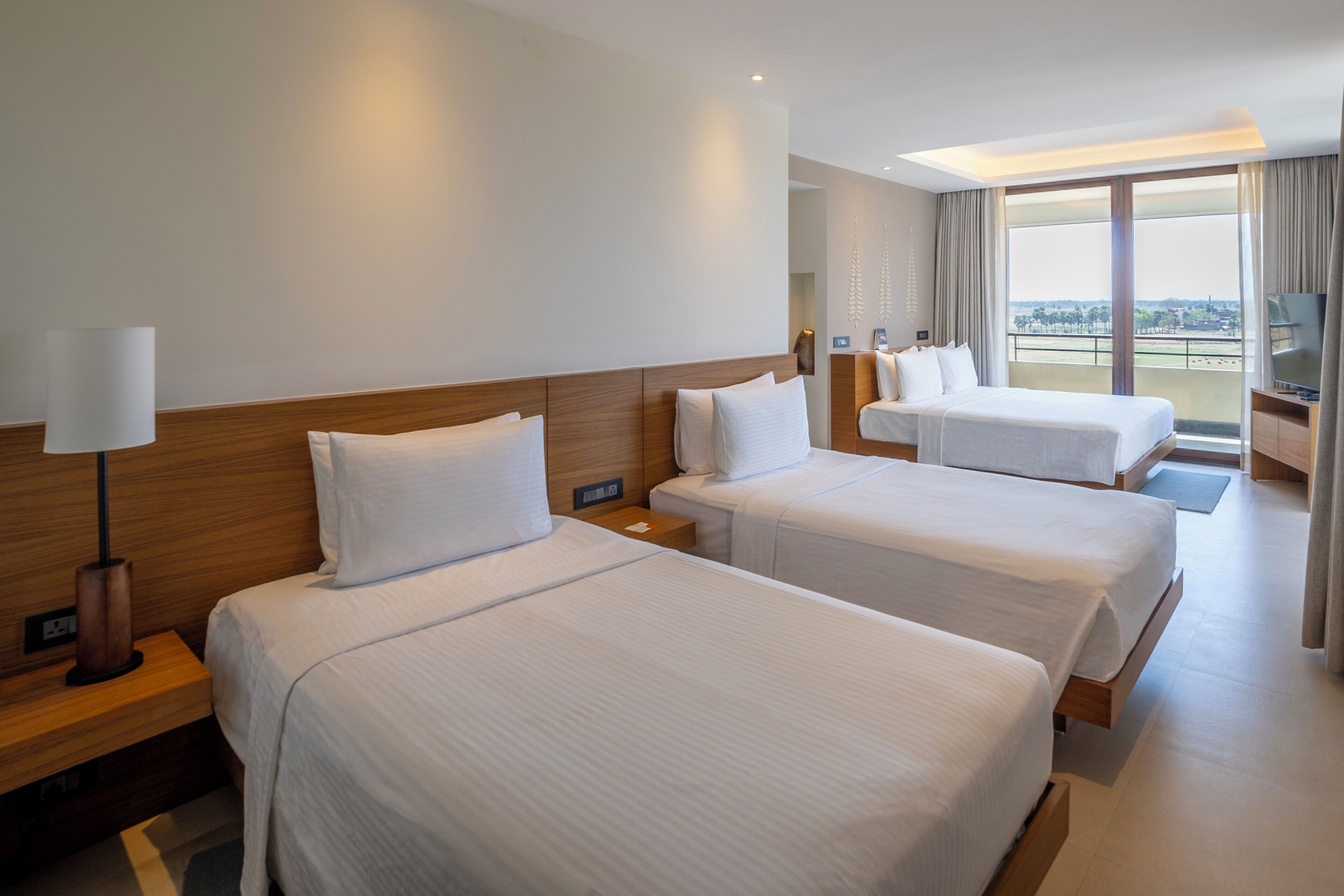 Ett hotellrum med två sängar, en TV och en balkong med utsikt över staden.