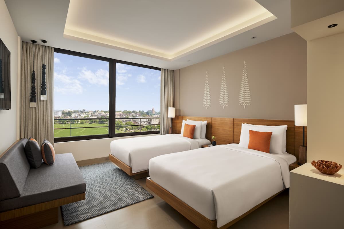 Een hotelkamer met twee bedden, een slaapbank en een groot raam met uitzicht op een stadsbeeld.