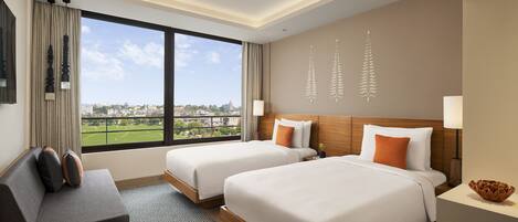 A hotel room with two beds, a sofa, and a large window offering a view of a cityscape.