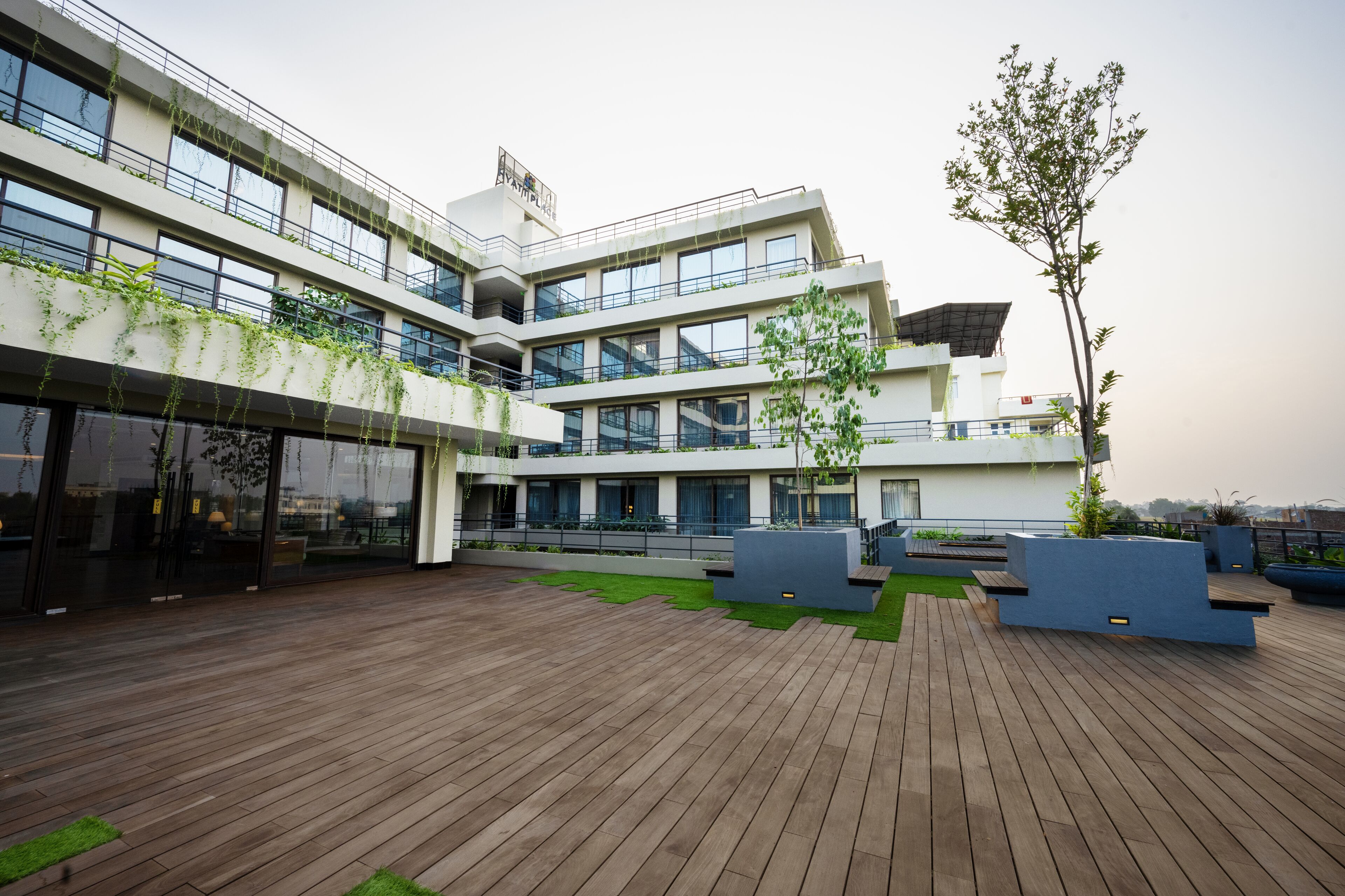 A modern building with multiple floors, large windows, and a wooden deck area with planters and seating.