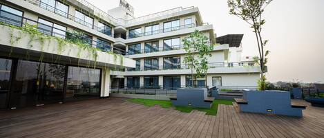 A modern building with multiple floors, large windows, and a wooden deck area with planters and seating.