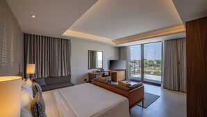 Habitación de hotel moderna con una cama grande, un escritorio, un televisor y un balcón con cortinas.