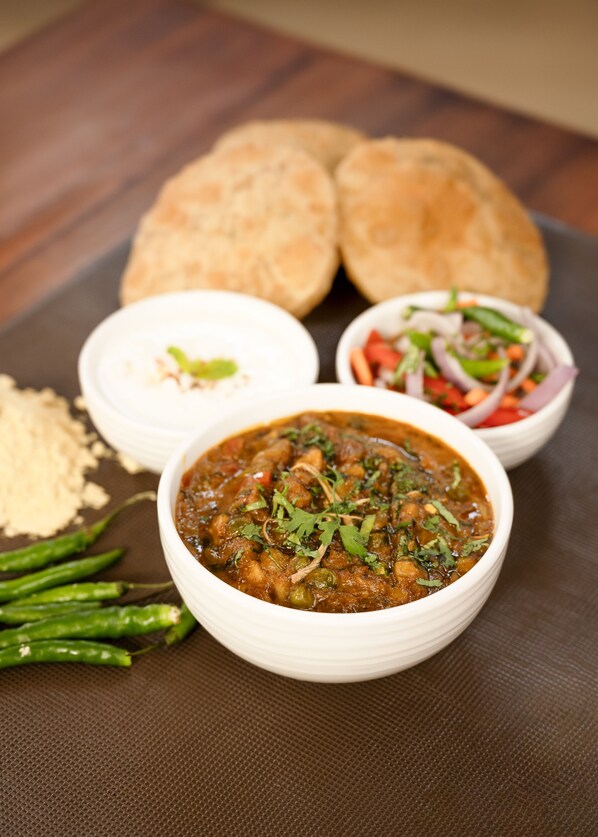 A meal consisting of a bowl of curry, two pieces of bread, a bowl of salad, and a small dish of sauce.