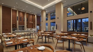 Un restaurante moderno con mesas y sillas de madera, una zona de bar central y amplios ventanales con vistas a la ciudad.